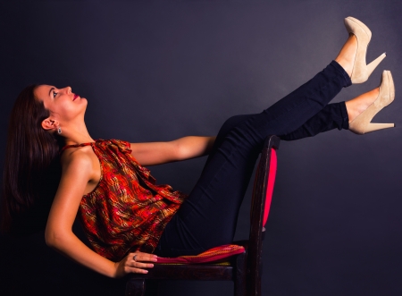 The portrait of a young brunette female sitting on a chair and leaning on her back  Isolated on grey の写真素材