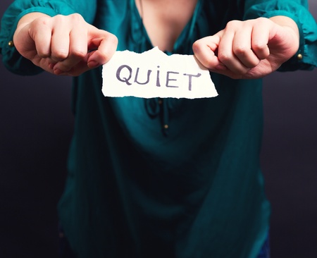 A girl holding a paper on which is written the word quiet の写真素材