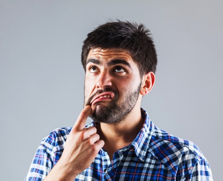 Funny young man is wondering while he pulling his lip downwards with finger - isolated on greyの写真素材