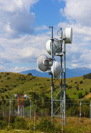 A closeup of a small telecommunication tower with mountains in the background.