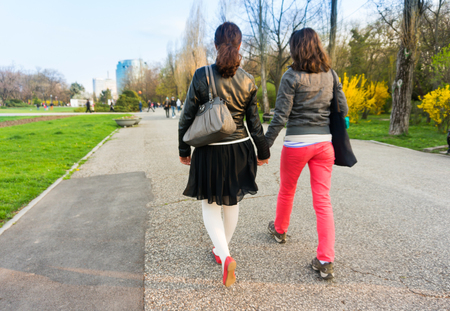Two young women are walking in the park holding hands togetherの写真素材