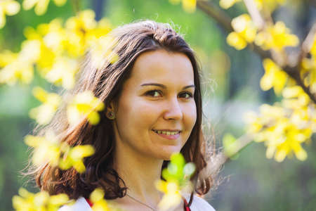 Smiling young brunette between yellow flowers in a park