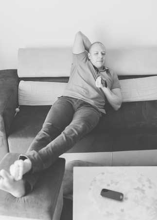 Young man lying on the couch and watching tv. Black and white photo.の写真素材