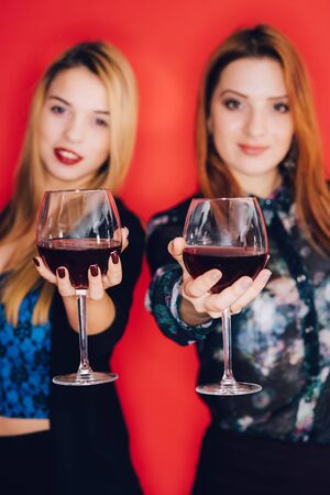 Two smiling woman holding glasses of red wine. Focus on the foreground. The women are in blur.の写真素材