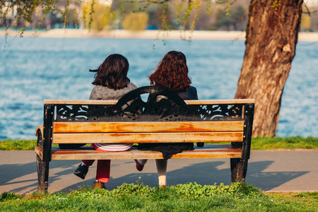 Two girls sitting on a wooden bench, resting and relaxingの写真素材