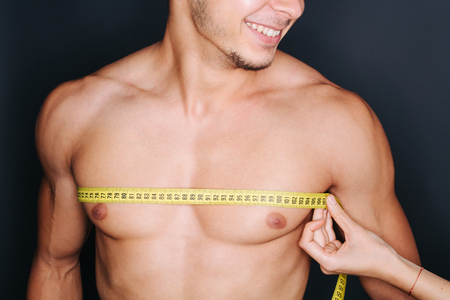 Muscular shirtless young man measuring chest and pecs with tape measureの写真素材