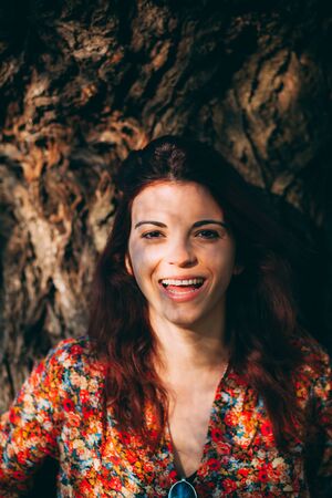 Happy young woman leaning against a tree, smilingの写真素材