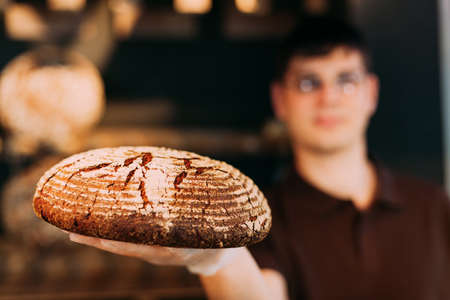 Shopkeepers in a bakery presenting round bread with wheat ears