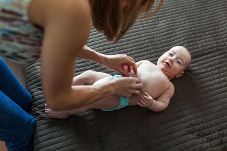 Woman changing her happy baby boy pamper while lying in bedの写真素材