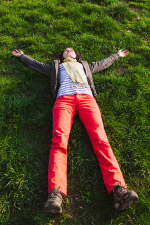Woman raising arms enjoying freshness of spring season while lying on grassの写真素材