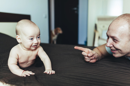 Young father pointing at his excited baby boy lying in bed