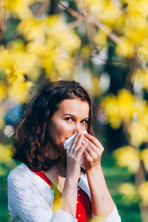 Closeup of a beautiful woman blowing her nose in parkの写真素材