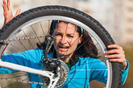 Baleful angry woman is trying to fix damaged bikeの写真素材