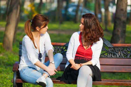 Two best friends talking outside, sitting on a bench in a parkの写真素材