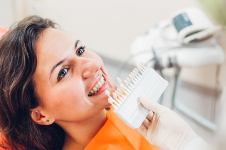Young smiling woman lying on dentist's chair and determining teeth's color  using shade guideの写真素材
