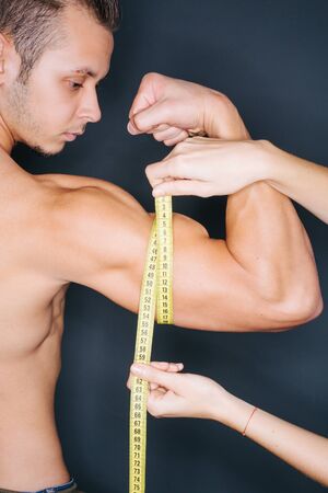 Woman hands measuring man's biceps with a tape