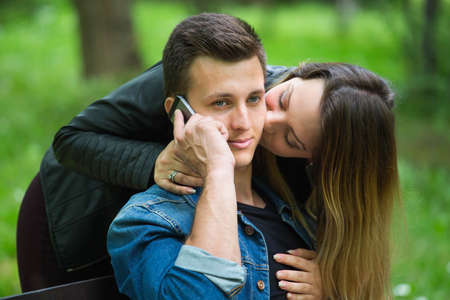 Young man using his mobile phone while being kissed by his girlfriend