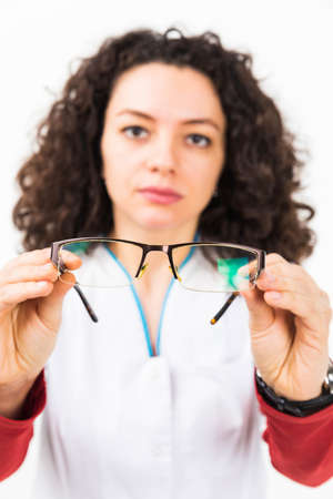 Blurry closeup of young woman ophthalmologist holding eyeglasses. Focus on the eyeglasses