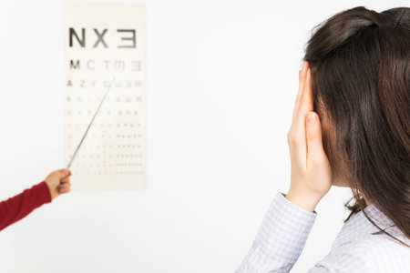 Woman covering one eye for ophthalmology exam and looking at eye chart - isolated on white.