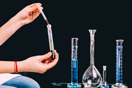 Hands holding a blood sample and different laboratory glassware with water and empty with reflection being againstの写真素材