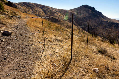 Fence made of barbed wire delimiting mountains covered in dried plants from a steppe climate.