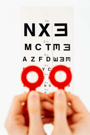 Blurry pose of hands holding two red frames with eye lenses in front of an eye chart - isolated on...