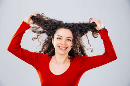Closeup of a happy woman smiling and holding her brown curls in handsの写真素材