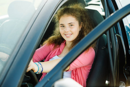 Young smiling girl is on the steering wheel while the car is stopped.