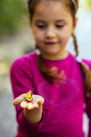 Blurry pose of a beautiful little girl holding a yellow butterfly. Focus on the butterflyの写真素材