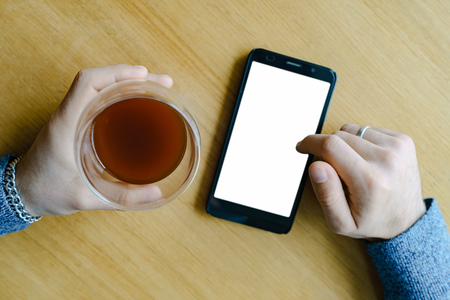 Male hand with coffee in glass and smartphone in cafe の写真素材