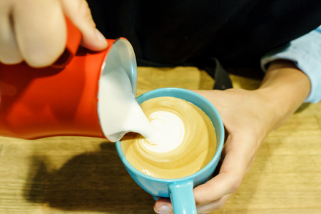 Barista in restaurant make cappuccino. Pouring milk into cup of coffee. Job concept.の写真素材