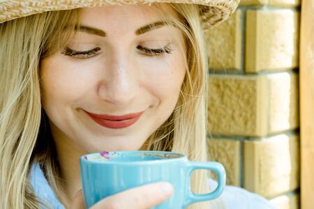 Happy beautiful blonde hair girl in jeans and hat holding a cup of cappuccino and looking into.の写真素材