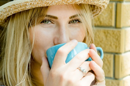 Pretty blonde hair beautiful girl happy looking into a camera and holding a cup of cappuccino in...