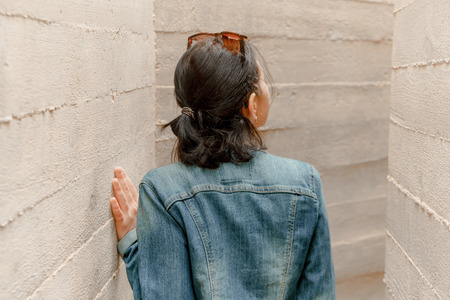 Attractive young woman stands between concrete walls. Caucasian girl in casual jeans looks up. Pretty fashion woman in outdoor space.の写真素材