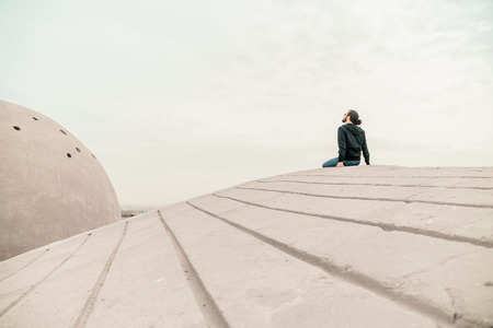 Side view unidentified young man in casual clothes and glasses sits on the high rock and looks at beautiful desert view and admires the natureの写真素材