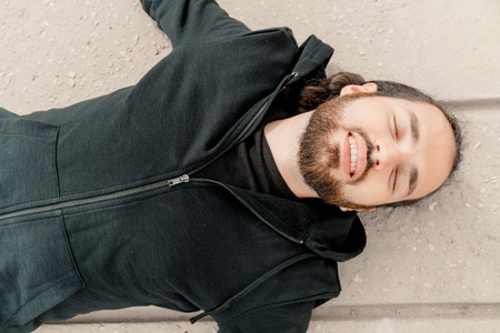 Close-up of cute young relaxed man in casual clothes lying with closed eyes on hill in nature and dreaming of somethingの写真素材