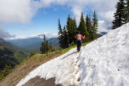 A female hiker navigates across some snow accumulation at the top of a mountain hike at Olympic National Park in Washington.の写真素材