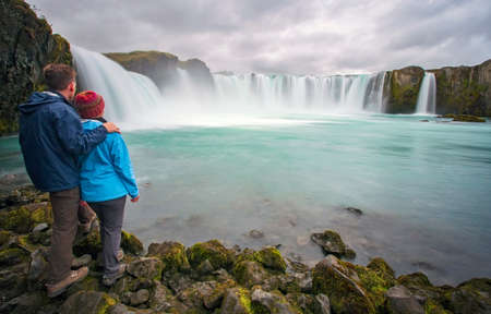 A couple stand together viewing GoÃ°afoss waterfall in Iceland.の写真素材