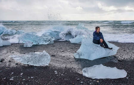 A female tourist sitting on a glacial ice chunk at JÃ¶kulsÃ¡rlÃ³n Beach in Iceland.の写真素材