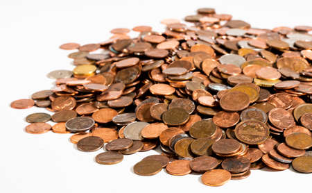 A large pile of old, dirty coins - mostly American pennies - on a clean white surface under bright lighting. Shallow macro depth-of-field shows the nearest coins in sharp focus, with farther coins gradually fading from clear view.の写真素材
