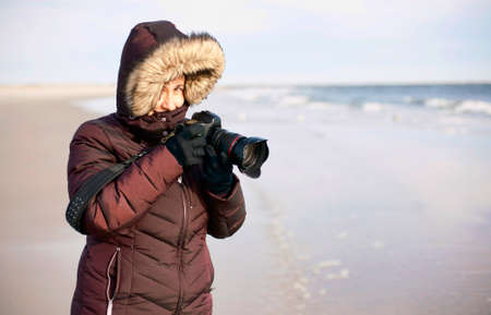 A female photographer smiles while holding her camera on a cold beach.の写真素材