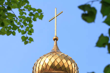 Golden dome of church with cross against blue sky in green birch leaves. Christian Orthodox religion. Trinity holidayの写真素材