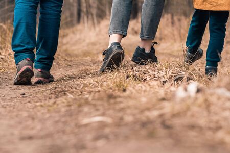 Family walks with children in forest path. Rear view on legs and shoes hikers. Walking boots and...