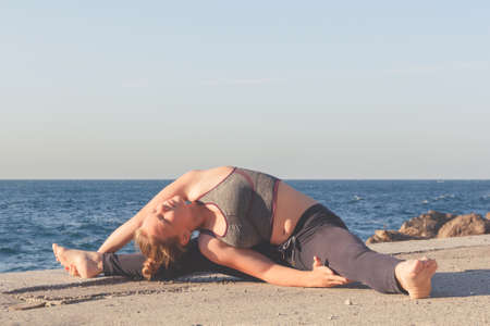Sporty young girl doing body stretching on sea background and blue sky. Cute gymnast girl yoga on...