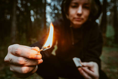 Teenage bully in hood holds burning match in his hand. Forest arsonist. Fire danger. Concept of arson and flame in night.の写真素材