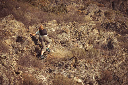 Young girl with backpack climbing on the high rock in the mountains. Adventure and extreme sport concept. Summer mountaineering or alpinism alone. Risk, adrenaline and freedom. Steep climbの写真素材