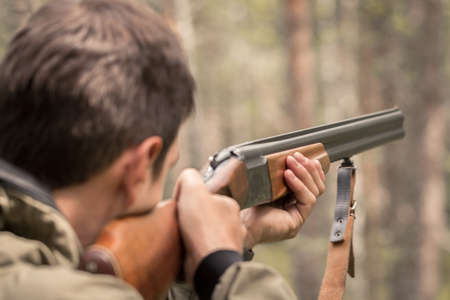 The hunter takes aim and is ready to shoot from a double barreled shotgun. Huntsman in the forest waiting for prey. Targeted rifle in the hands of a poacher.の写真素材