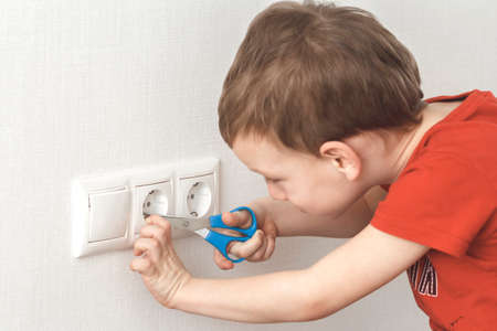 Little boy plays with electric socket and scissors. High voltage hazard.
