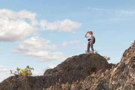 Hiker girl with backpack standing on top of mountain. Tourist looks from peak of hill to beautiful...