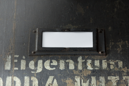view on the front of an old wooden case for military equipment with metal fittings and a stencilled german words and an empty title block with space for your text- bright light moodの写真素材